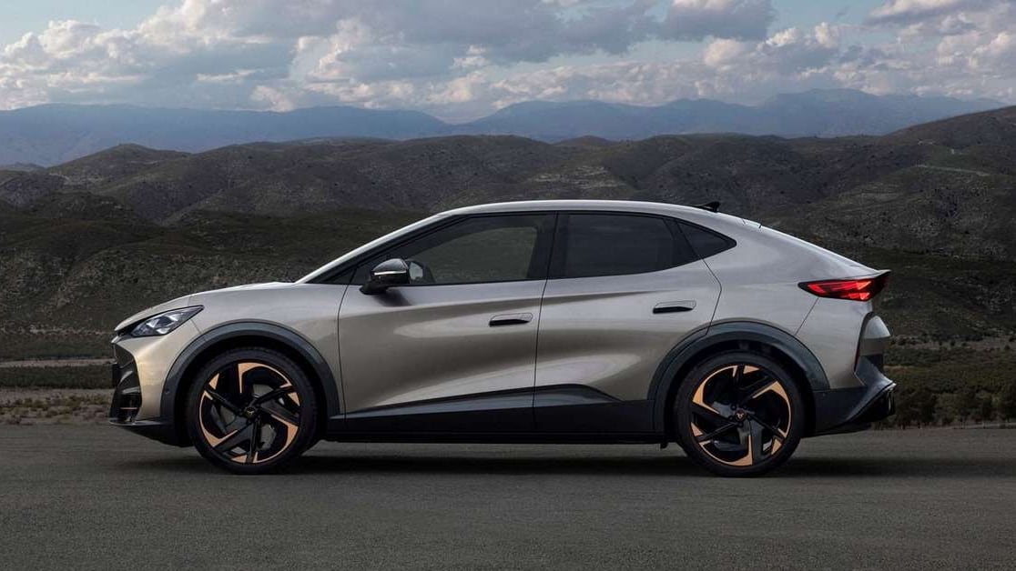 The electric CUPRA Tavascan in side profile, graphite body and copper wheel inserts, with a mountain range behind it