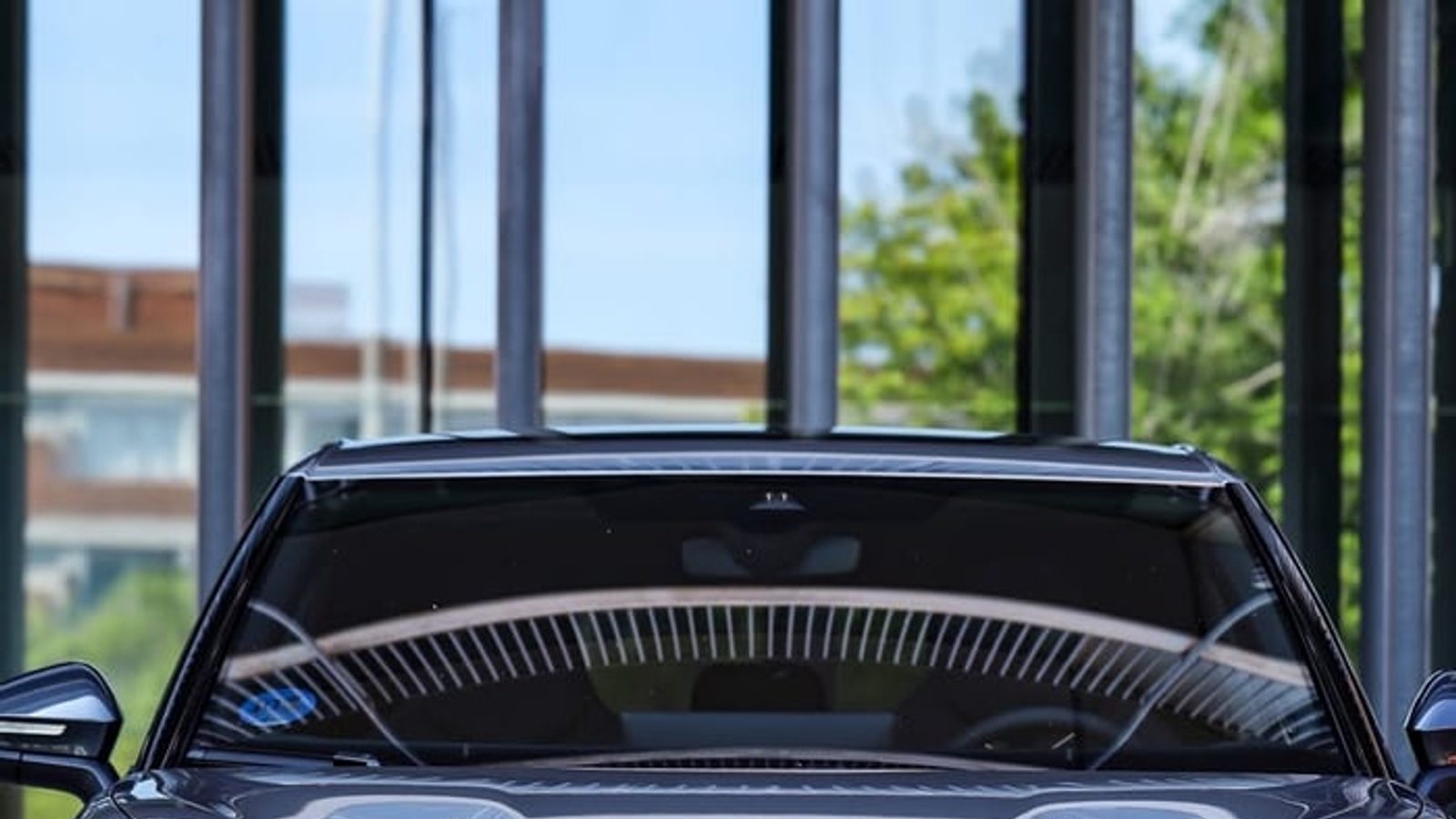 The CUPRA Tavascan from the front, in a portrait crop, in front of a glass-and-steel building